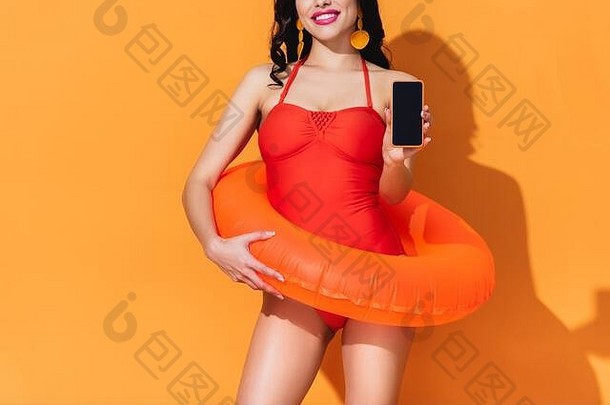 裁剪视图快乐女人泳衣充气环持有智能手机空白屏幕橙色