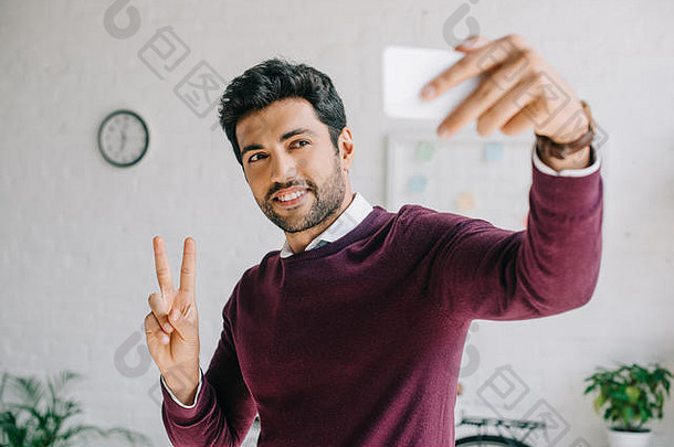 微笑商人勃艮第毛衣采取自拍智能手机显示手指办公室