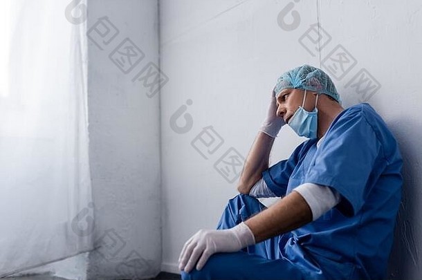 累了成熟的医生医疗帽护目镜坐着白色墙诊所