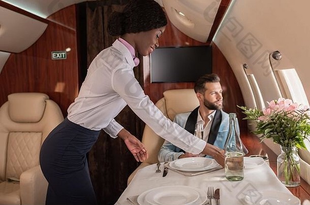 微笑漂亮的非洲美国空姐设置表格私人飞机优雅的男人。