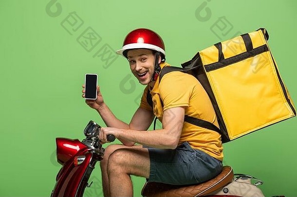 一边视图快乐交付男人。黄色的统一的背包显示智能手机空白屏幕踏板车孤立的绿色