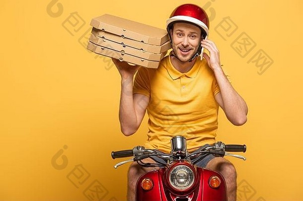微笑交付男人。黄色的统一的骑踏板车披萨盒子会说话的智能手机孤立的黄色的