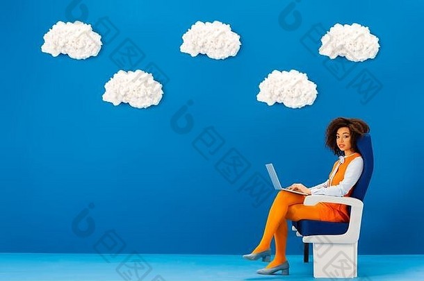 非洲美国复古的衣服坐着座位持有移动PC蓝色的背景云