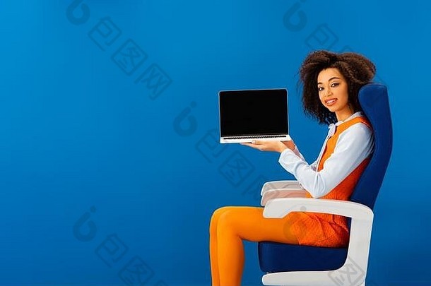 微笑非洲美国坐着座位持有移动PC孤立的蓝色的