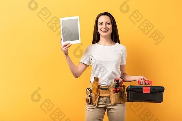 微笑勤杂女持有数字平板电脑工具箱黄色的背景