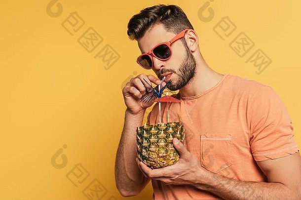 自信年轻的男人。太阳镜喝新鲜的鸡尾酒一半新鲜的菠萝黄色的背景