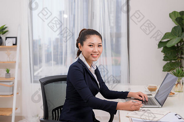 有吸引力的快乐的年轻的女商人工作移动PC微笑坐着桌子上明亮的现代办公室