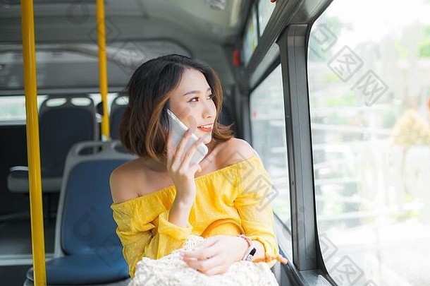 年轻的亚洲女人智能手机坐着公共汽车