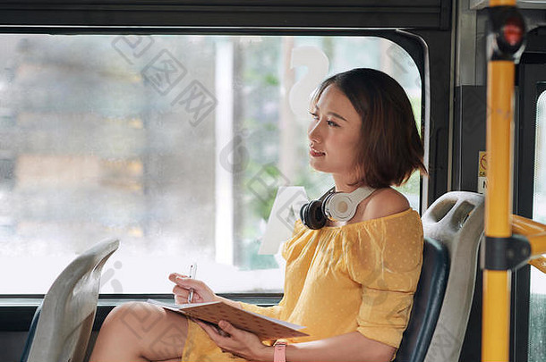 美丽的年轻的女人坐着城市公共汽车写作笔记笔记本