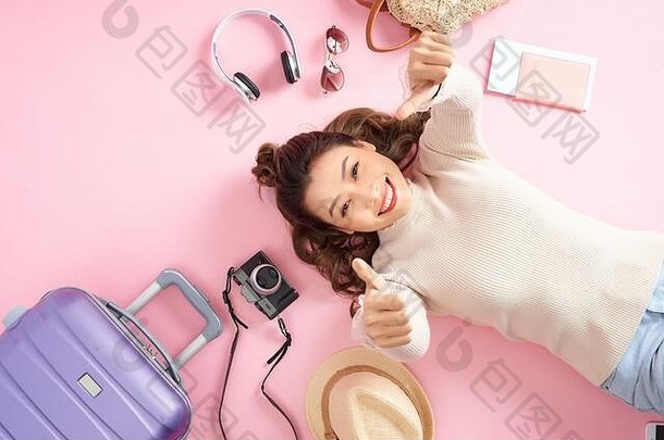 美女人微笑幸福的显示拇指粉红色的地板上说谎旅行行李前视图