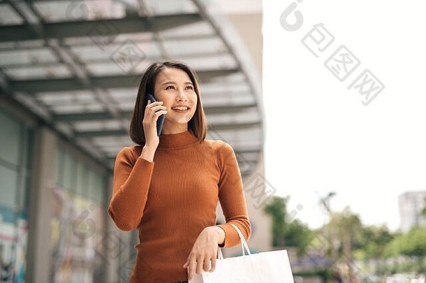肖像快乐年轻的亚洲女人会说话的移动携带纸购物袋走户外购物中心
