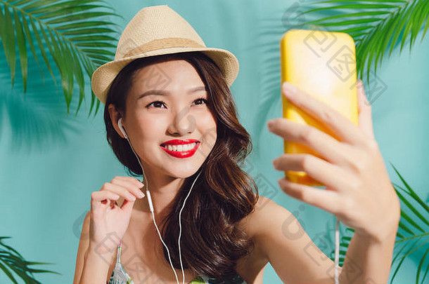漂亮的微笑亚洲女人智能手机自拍照片站蓝色的背景