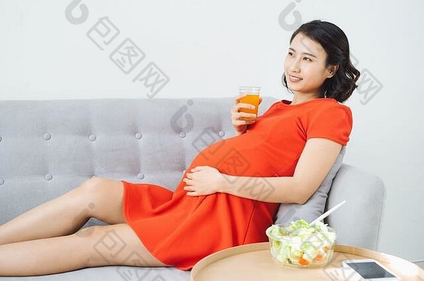 漂亮的年轻的亚洲怀孕了女人吃沙拉喝牛奶坐着沙发