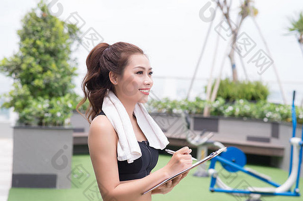 有吸引力的女健身房教练采取笔记站在户外公园