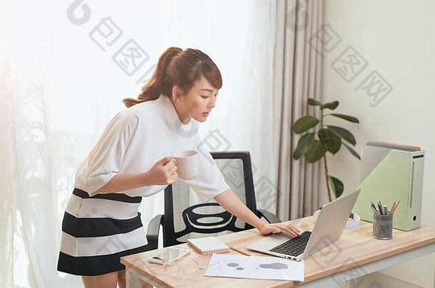 美丽的年轻的亚洲女人移动PC持有杯茶办公室