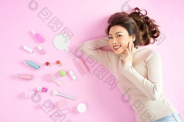 漂亮的亚洲女人微笑说谎粉红色的地板上化妆品化妆工具前视图