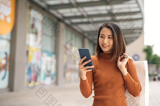 肖像优雅的年轻的亚洲女人持有购物袋智能手机离开购物中心