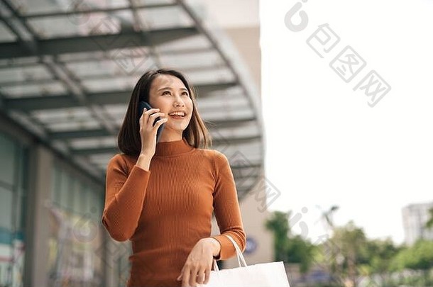 肖像快乐年轻的亚洲女人会说话的移动携带纸购物袋走户外购物中心