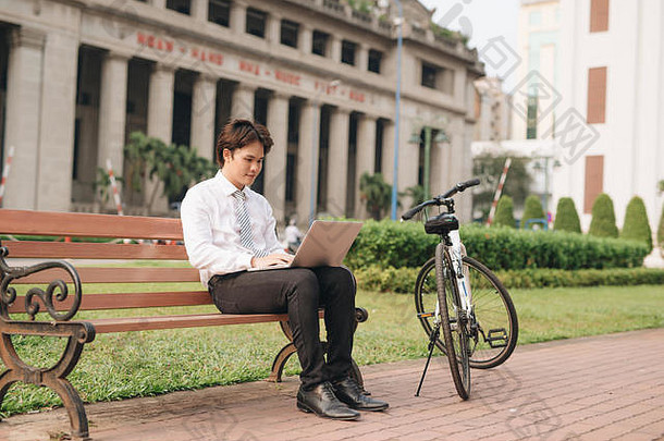 年轻的英俊的商人移动PC自行车坐着板凳上公园