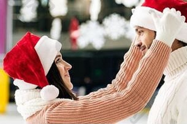 全景拍摄美丽的快乐夫妇圣诞老人帽子支出时间滑冰溜冰场