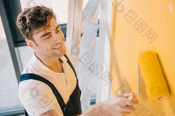 英俊的年轻的画家微笑绘画墙黄色的颜色油漆辊