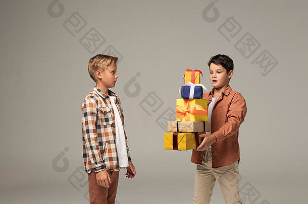 惊讶男孩持有堆栈五彩缤纷的礼物盒子惊讶哥哥孤立的灰色
