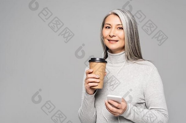 快乐亚洲女人高领毛衣咖啡听音乐耳机智能手机孤立的灰色
