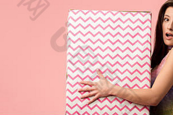 全景拍摄震惊了年轻的时尚的迪斯科女孩持有巨大的礼物盒子孤立的粉红色的