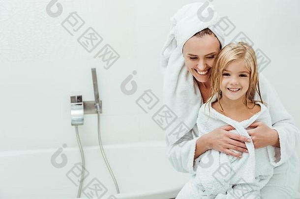快乐妈妈。微笑拥抱可爱的女儿浴袍
