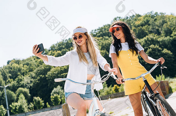 快乐金发女郎浅黑肤色的女人女孩骑自行车采取自拍夏天