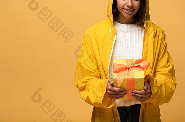 裁剪视图微笑女人黄色的雨衣持有礼物盒子孤立的黄色的