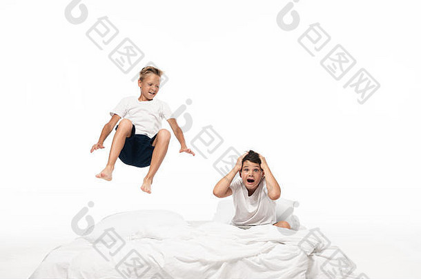 快乐的男孩悬浮震惊了哥哥坐着床上用品持有手头孤立的白色