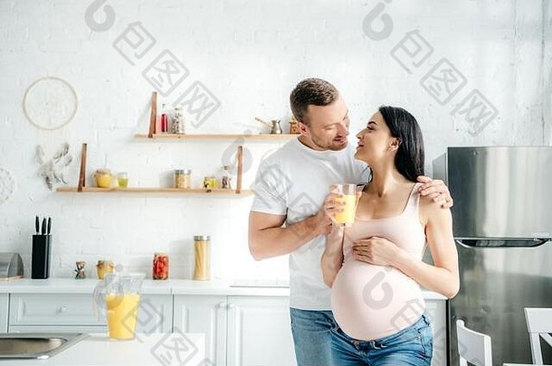快乐的怀孕了夫妇持有橙色汁厨房