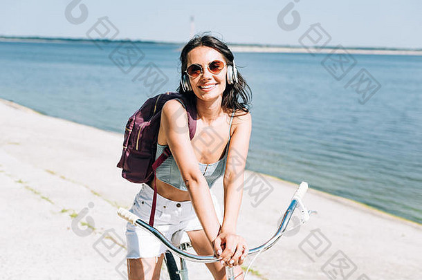 微笑<strong>女孩</strong>背包骑自行车听音乐耳机河夏天