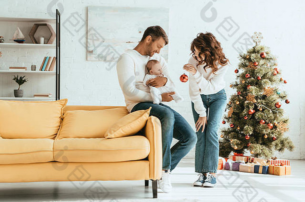 有吸引力的女人显示圣诞节球孩子坐着父亲手装饰圣诞节树