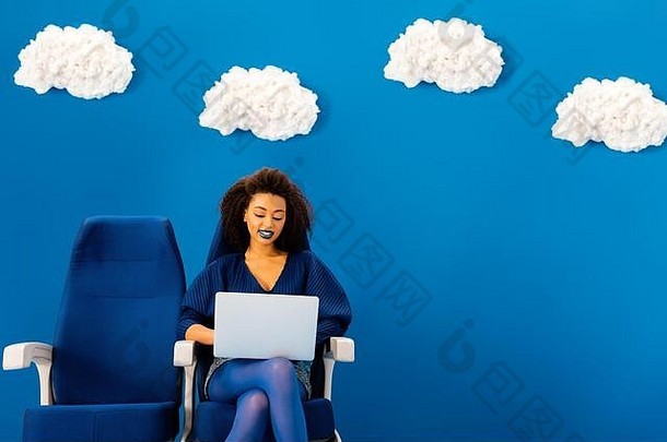 微笑非洲美国坐着座位移动PC蓝色的背景云