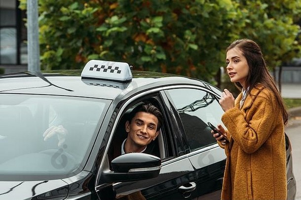 年轻的女人持有智能手机会说话的微笑出租车司机