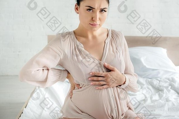 担<strong>心怀</strong>孕了年轻的女人睡衣感觉疼痛触碰肚子坐着床上