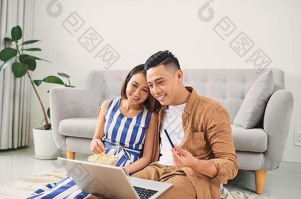 年轻的亚洲夫妇看视频移动PC生活房间
