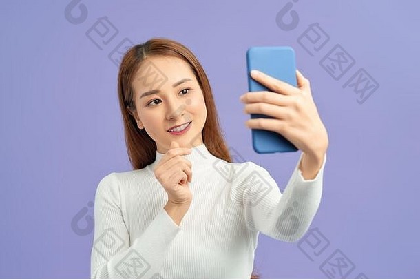 微笑年轻的女孩使自拍照片智能手机紫罗兰色的背景