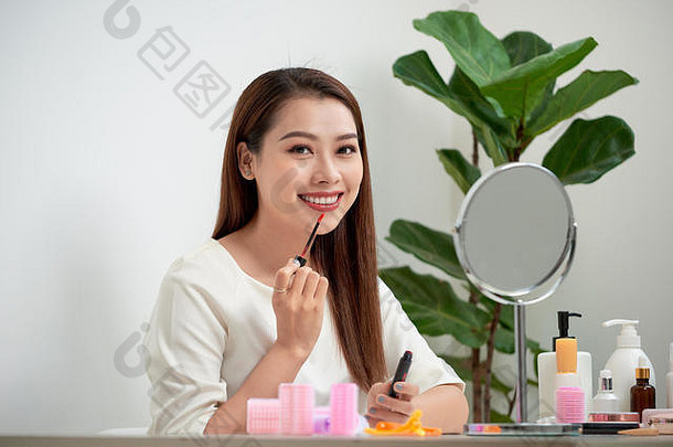 年轻的美丽的女人使化妆镜子坐着桌子上