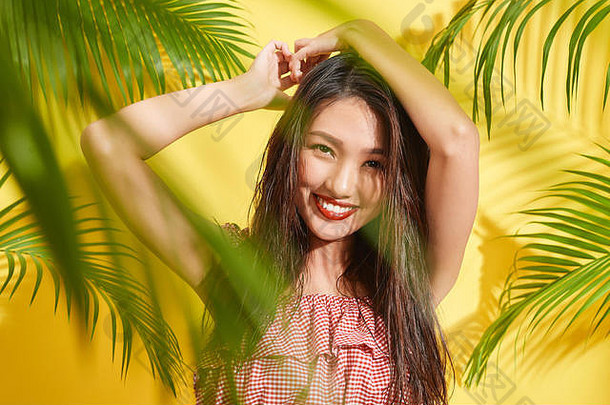 美丽的女孩湿头发站棕榈叶子黄色的背景