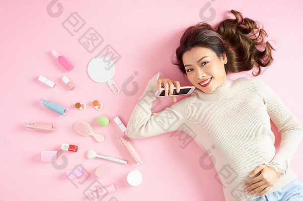年轻的亚洲美丽的女人显示聪明的电话化妆品化妆工具说谎粉红色的地板上前视图