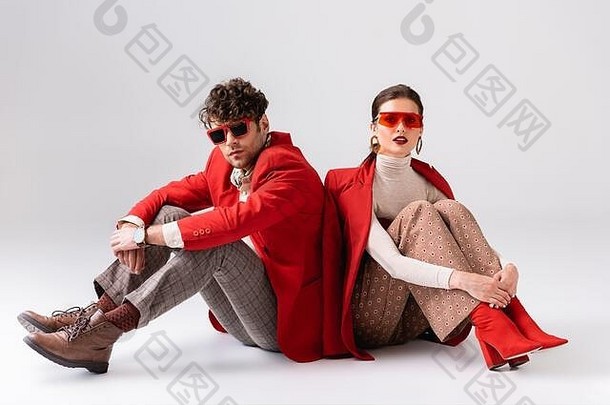 时尚夫妇红色的开拓者太阳镜坐着地板上摆姿势灰色
