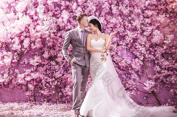 浪漫的新郎接吻新娘额头站墙覆盖粉红色的花
