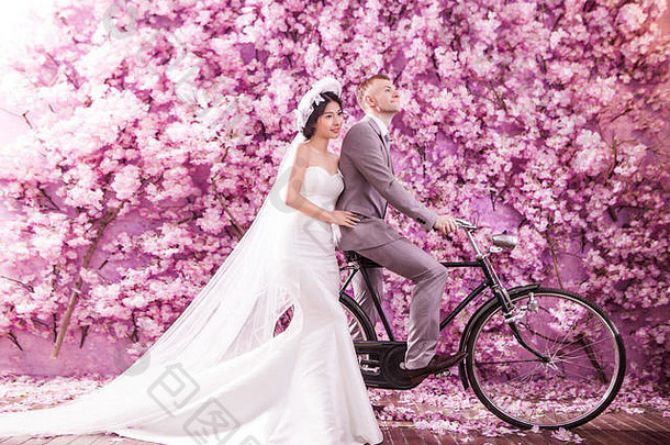 深思熟虑的新娘站新郎骑自行车粉红色的花覆盖墙