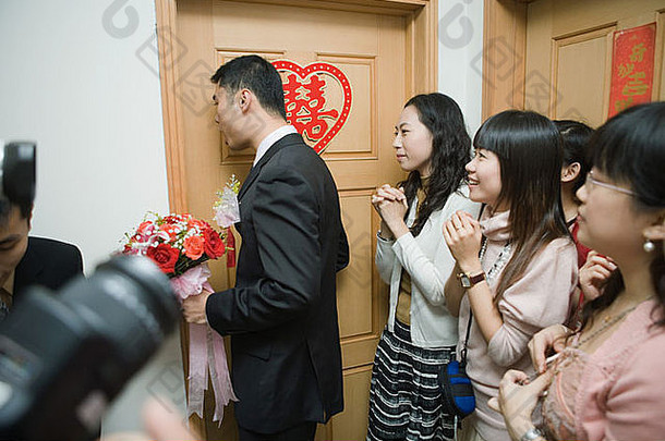 中国人婚礼新郎持有花束敲门新娘的通过新娘的朋友看