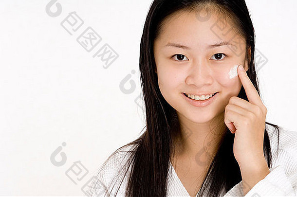 年轻的中国人女孩浴袍应用脸奶油