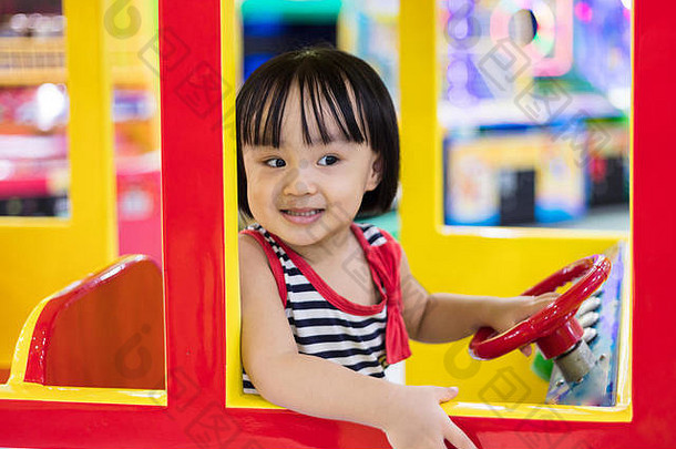 快乐亚洲中国人女孩开车玩具公共汽车室内操场上
