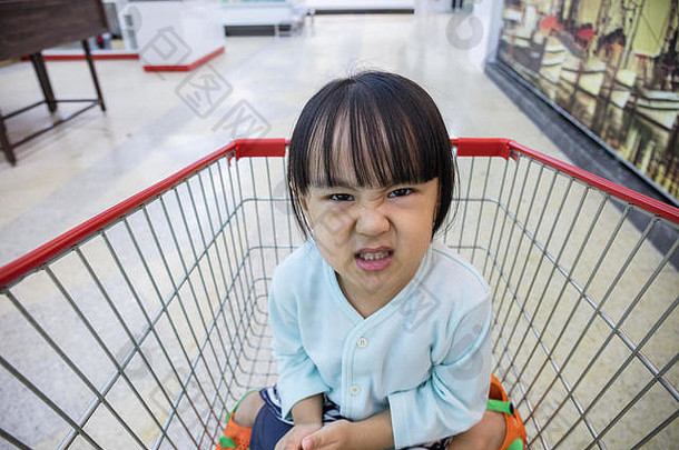 快乐亚洲中国人女孩坐着购物车超市